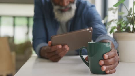 Video-of-african-american-senior-man-drinking-coffee-and-using-tablet