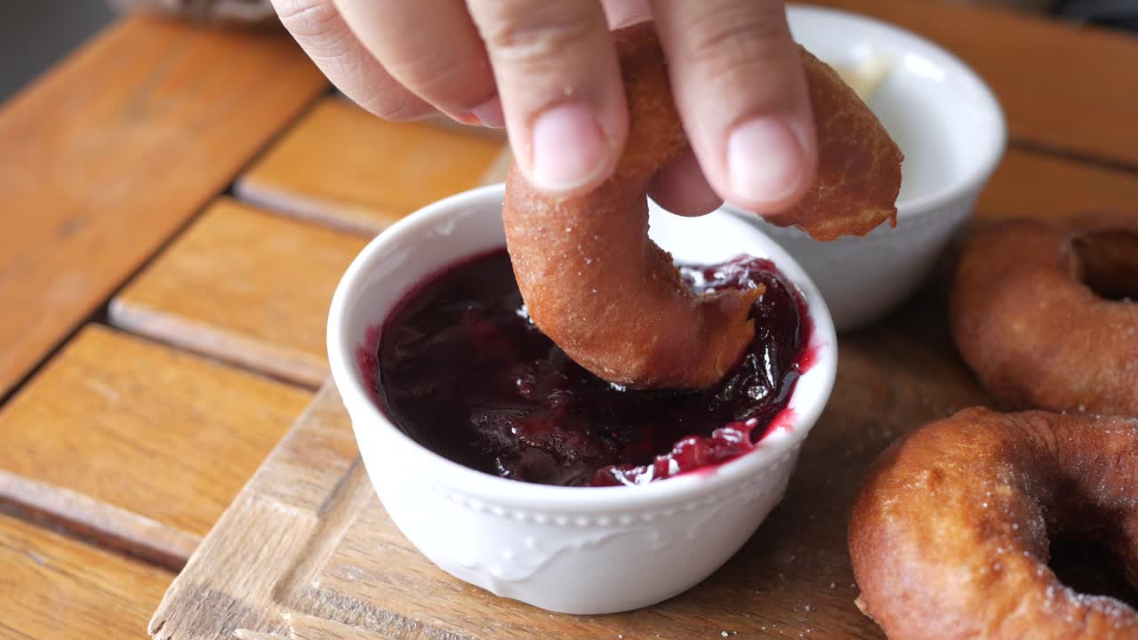 Hand dipping donut in jam