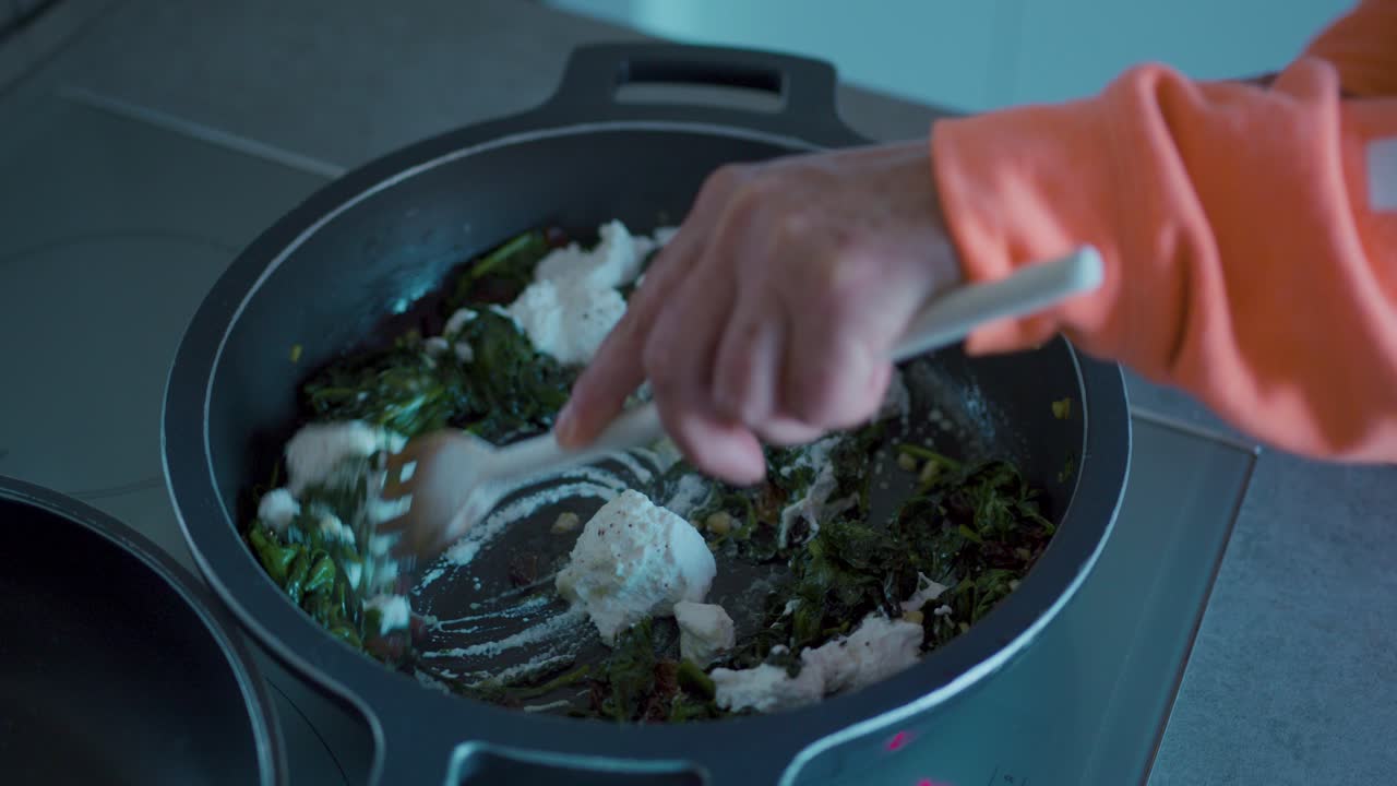 Stirring spinach with cheese and raisins in a frying pan using a wooden spatula