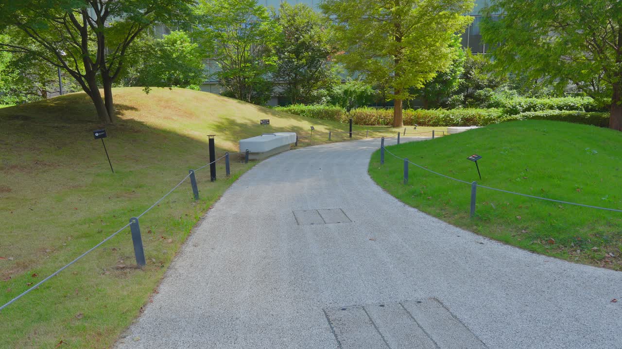An eye-level shot of a curving gravel pathway bordered by grassy slopes and modern lighting in a tranquil urban park