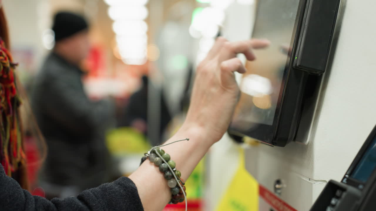 Person interacting with a touchscreen interface on a machine, about to make a payment. showing blurry people in the background