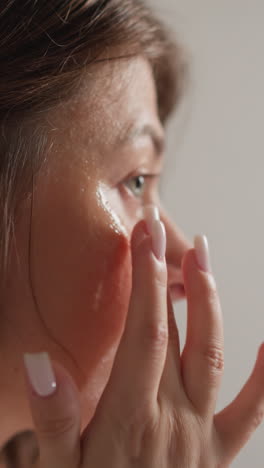 una mujer morena frota la máscara facial con las puntas de los dedos en un primer plano de la ducha. una mujer con cabello oscuro masajea la cara con crema nutritiva transparente en cámara lenta