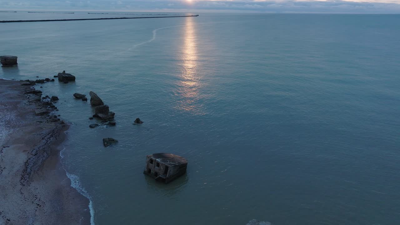 hermosa vista aérea que establece las ruinas de la fortificación de la costa de hormigón de karosta, vibrante puesta de sol de alto contraste sobre el tranquilo mar báltico, noche de invierno, amplio disparo de drones avanzando, inclinado hacia arriba
