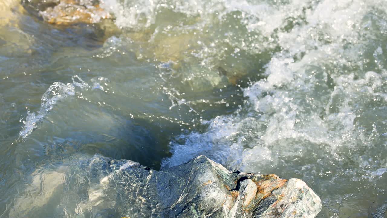 Clear water flows over rocks in a natural stream, creating dynamic movement and texture under bright daylight