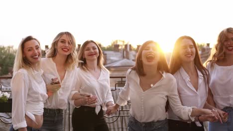 Happy-smiling-outside-on-a-balcony-terrace.-Building,-city-landscape-background-jumping-together-in-slow-motion.-Having-fun-together,-fashionable-female-in-same-clothes-laughing.-Enjoyment-life