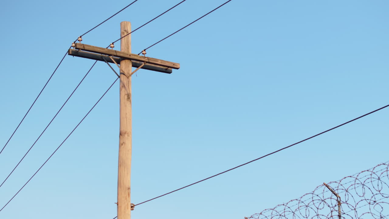 Aerial view of power lines and a barbed wire fence. Shot at sunrise against a blue sky.