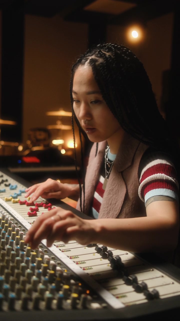 Asian Female Audio Technician Working at Mixing Console in Recording Studio