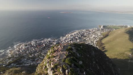 Hikers-on-top-of-Lion's-Head-in-Cape-Town-overlooking-the-city-and-ocean,-aerial-view