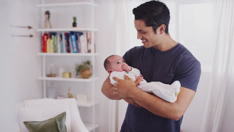 proud hispanic father holding his four month old child at home, waist up, close up