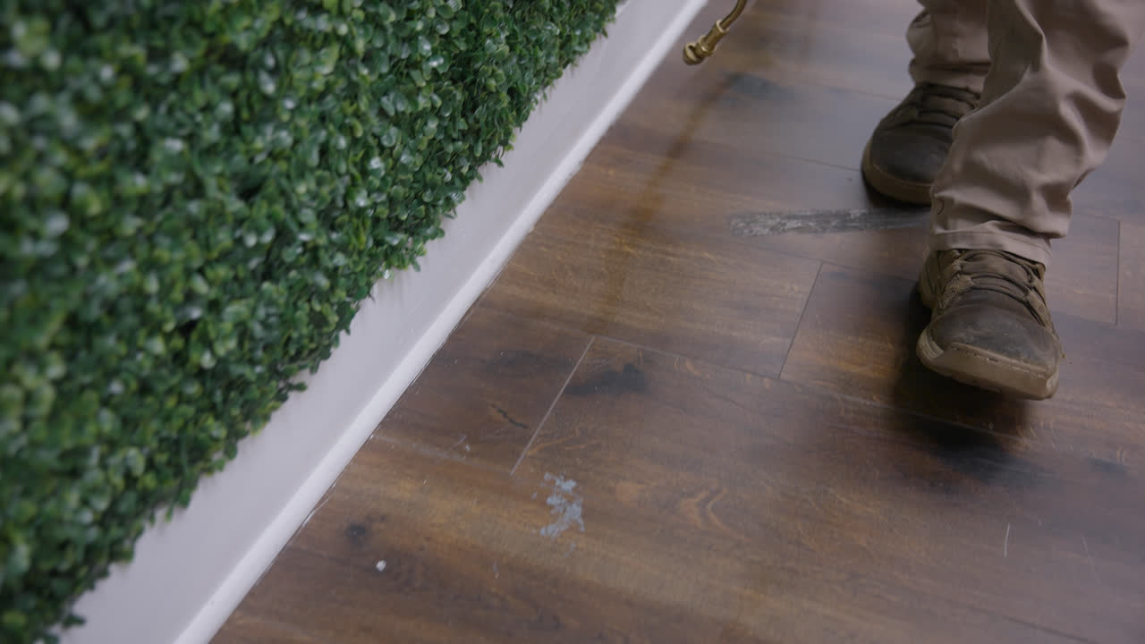 Close tracking of pest control application along office baseboards and flooring, mist wetting ground creating reflection