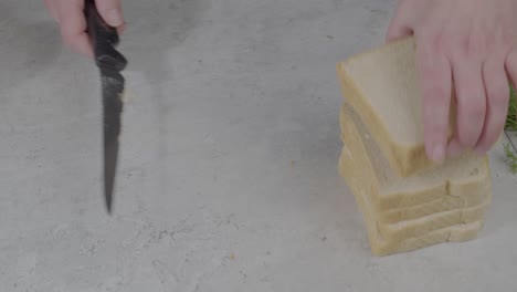 static shot of an individual cutting the crusts off of the slices of bread