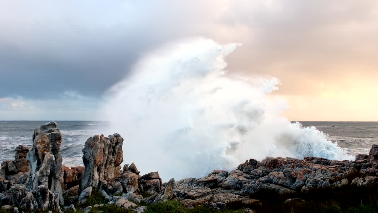 la ola choca dramáticamente en slomo y rocía agua de mar en las rocas costeras al atardecer.
