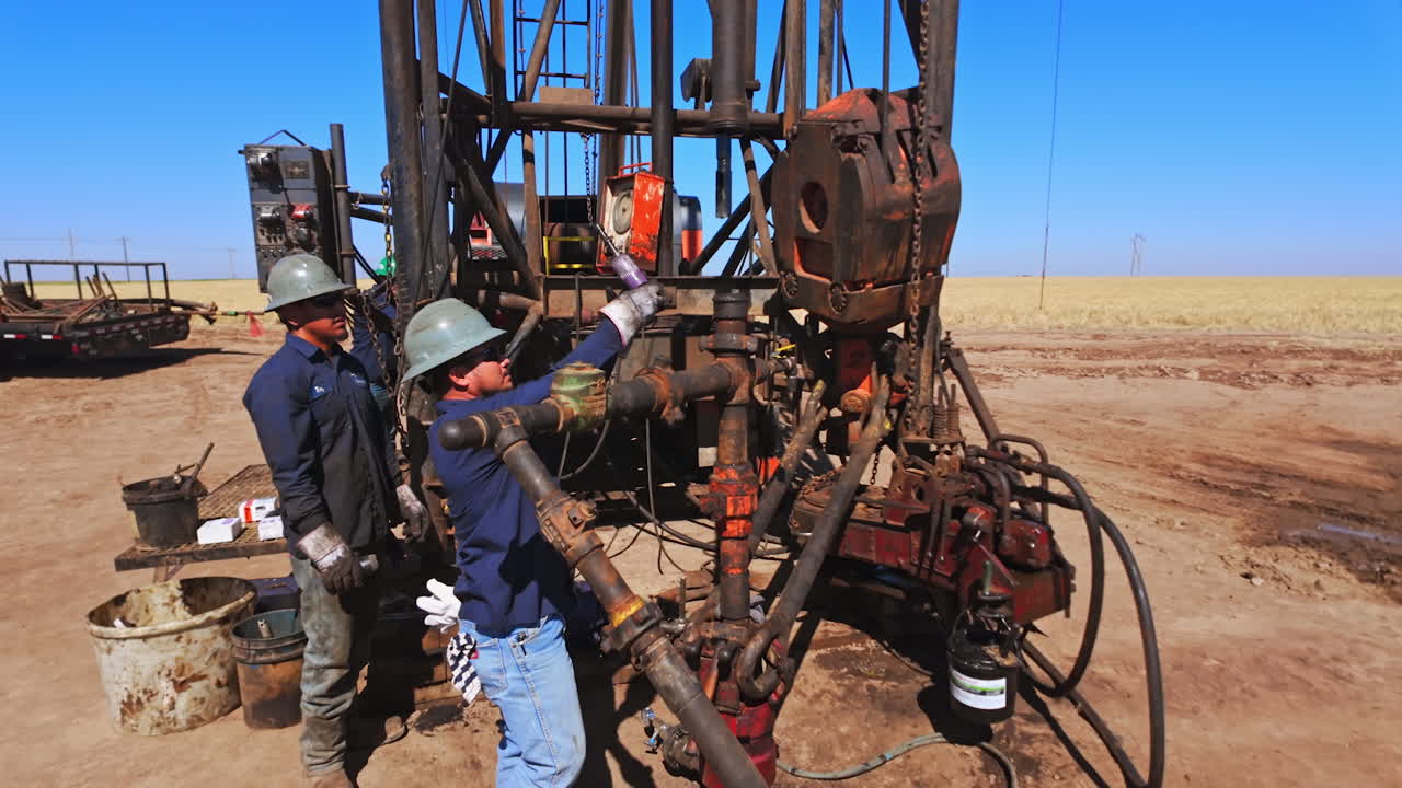 Three men wearing dirty uniforms and protective helmets work with the drilling equipment in the desert. Worker maintains the equipment for oil boring.