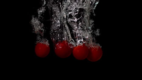 cherry tomatoes falling in water on black background