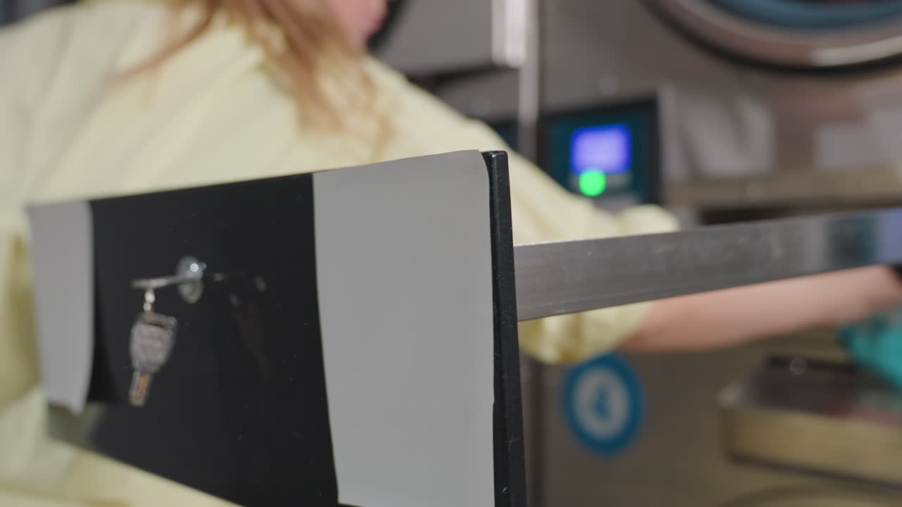 Professional operator cleans inner filter drawer of industrial washing machine with hand towel, close view of stainless dryers in row, routine maintenance for hygiene inside laundromat