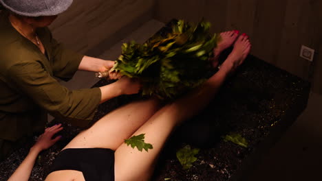 woman receiving banya treatment with oak leaves