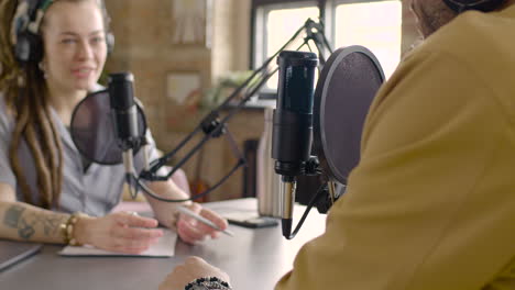 young man and woman sitting at a table with microphones while they recording a podcast