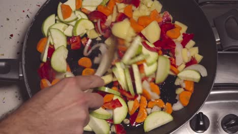Man stirs vegetables in frying pan for Spanish pisto with wooden spoon