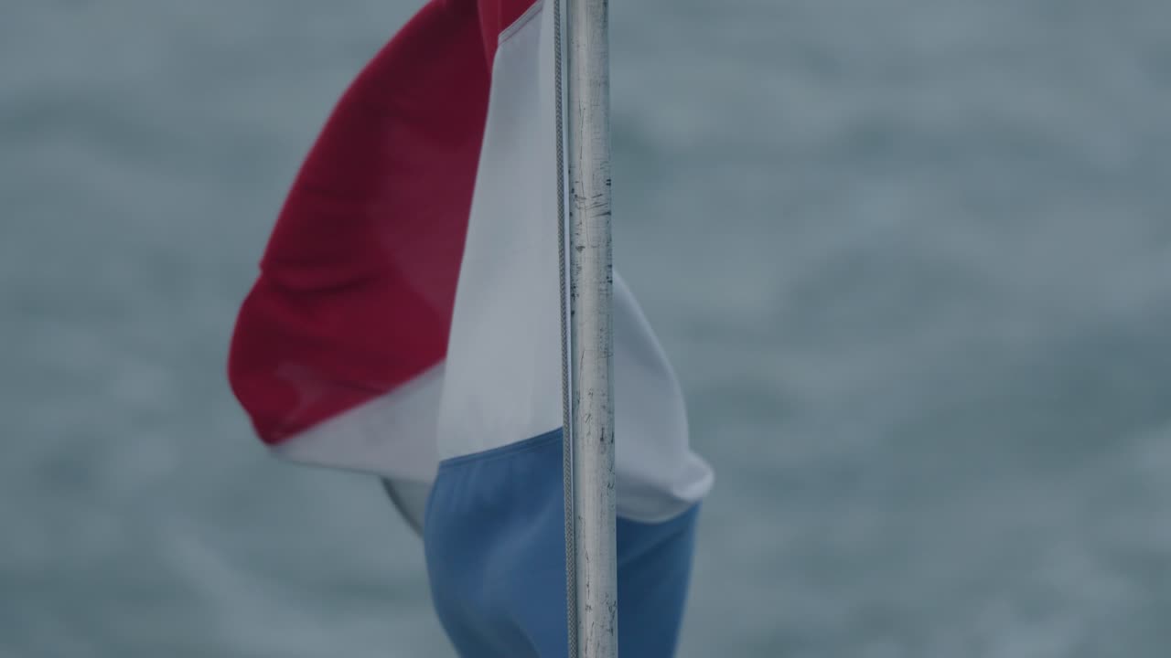 바람이 부는 조건에서 졸졸 흐르는 네덜란드 국기의 슬로우 모션 아래쪽 기울기 샷