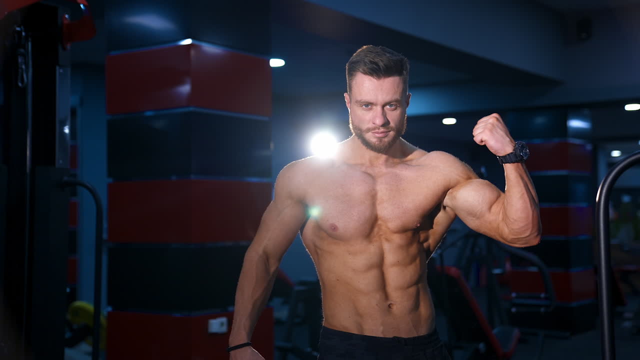 Athletic man posing to camera. Handsome man with naked torso showing his muscular body. Bodybuilder with trained biceps in sports center.