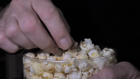 a man's hand takes popcorn out of a plastic bucket and watches tv at home