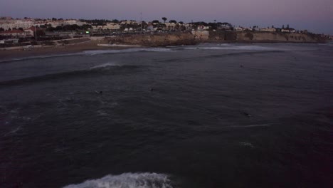 surfer takes off riding long board wave in san pedro cascais, aerial tracking at dusk