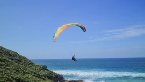 paragliding flight scene in front of the beach with rocks mountains and sand with people having fun in the flight with sea waves air sport