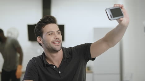 smiling man making selfie on phone at open kitchen. young guy holding phone.