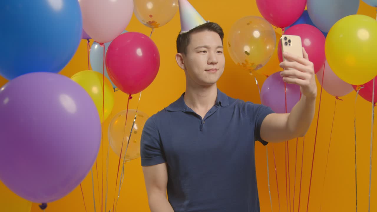 셀피를 찍고 파티 모자를 입고 풍선으로 둘러싸인 생일을 축하하는 남자의 스튜디오 초상화