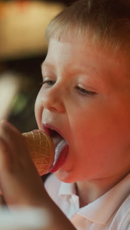 toddler boy licks chocolate ice cream held by mother hand in cafe slow motion. funny little son eats sundae with parent in restaurant closeup