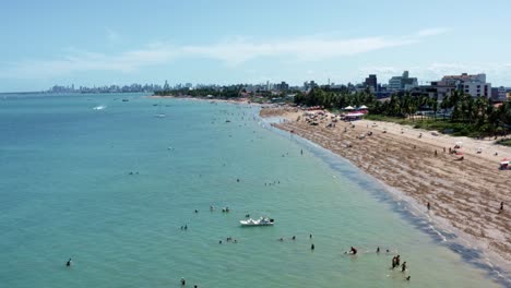tilt up aerial shot of bessa beach during low tide in the tropical capital city of joao pessoa, paraiba, brazil with people enjoying the ocean and fishing boats at shore on a summer day