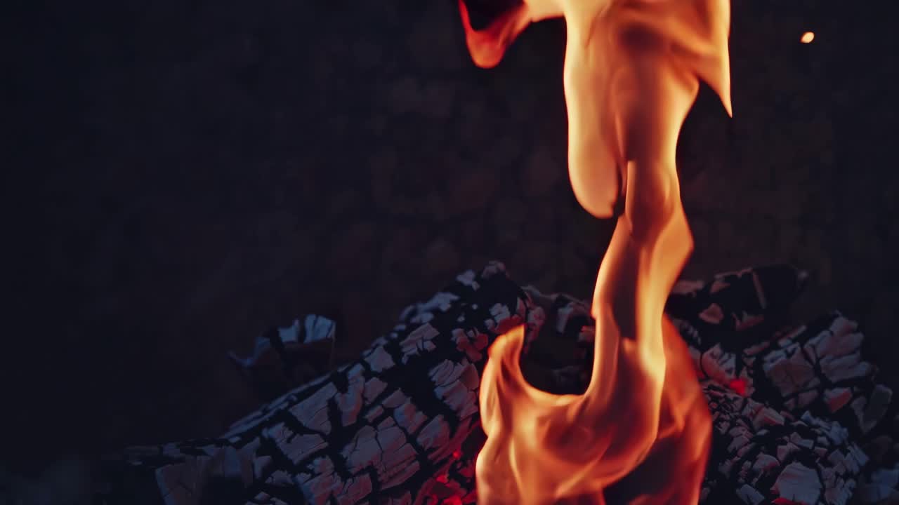Nærbillede video af et lejrbål, der viser flammer, der danser over forkullede træstammer