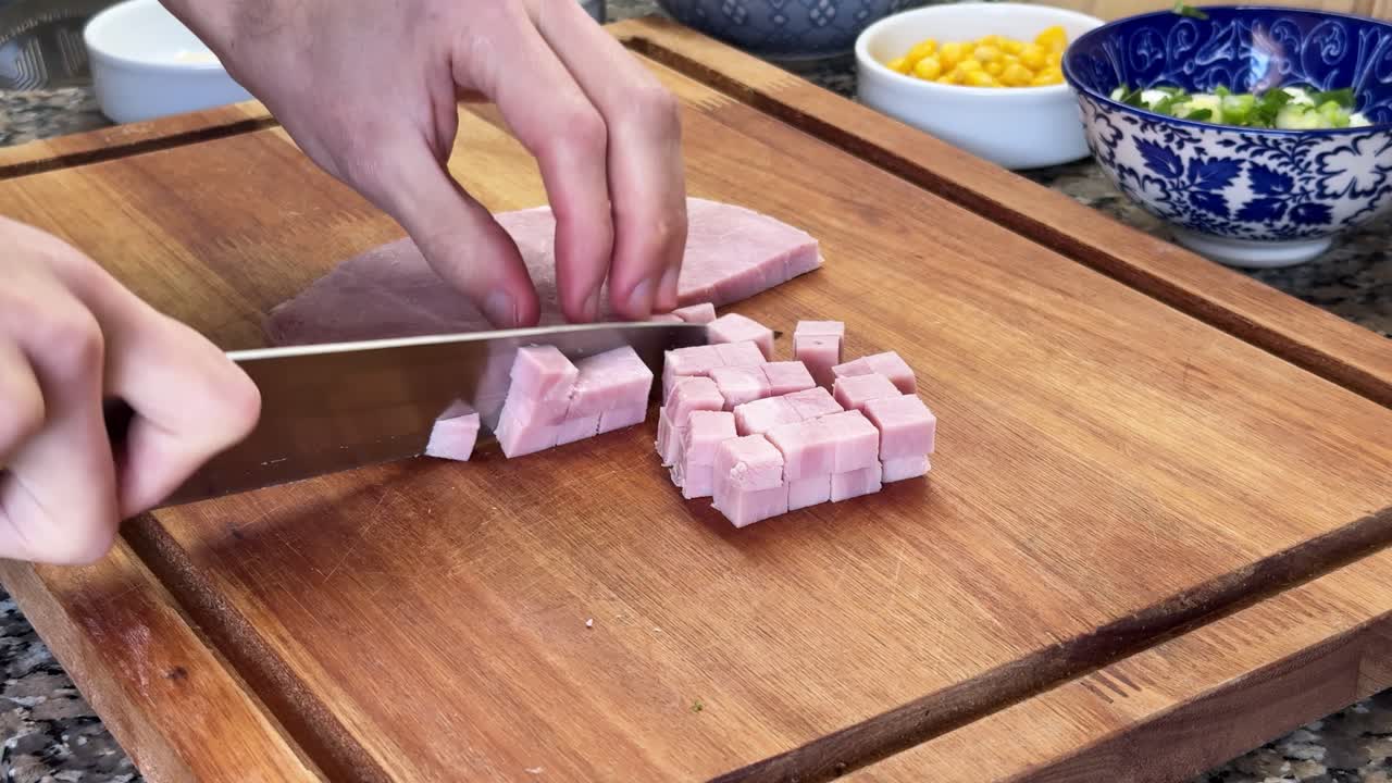 Person dicing ham on a wooden cutting board