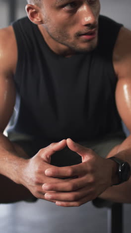 vertical video: resting after intense workout, sweaty man sitting and catching breath in gym