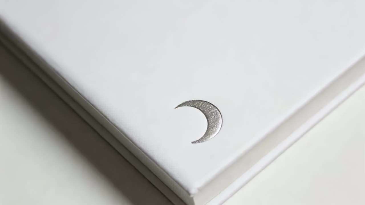 Moving camera zooming on diagonal white notebook stack on tabletop, highlighting silver crescent