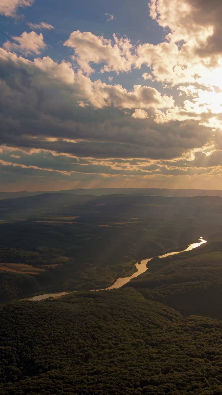 Aerial video view of a winding river through lush hills under a dramatic sky, capturing serene