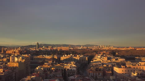 Backwards-fly-above-buildings-in-urban-borough-at-golden-hour.-City-lit-by-bright-low-sun-before-sunset.-Barcelona,-Spain