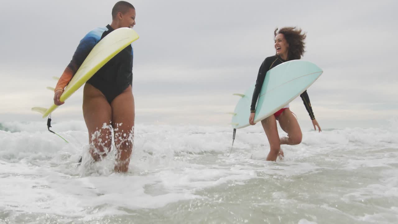 felices amigas afroamericanas corriendo fuera del mar con tablas de surf