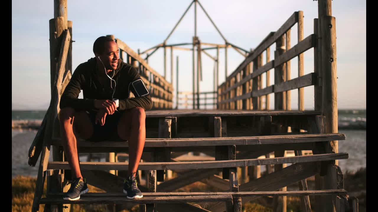 corredor afroamericano sentado en el muelle y usando un reloj inteligente 4k