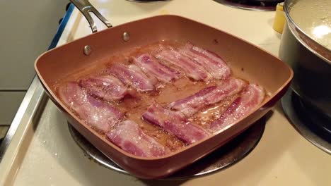 uncured bacon cooking in a square pan on an electric stove