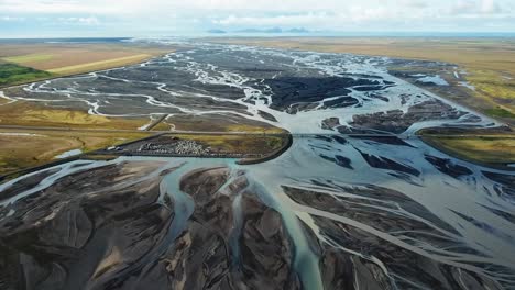 aerial view capturing a glacial river winding through icelandic plains, forming intricate patterns of water and sediment against a backdrop of mountains and clouds, near seljalandsfoss waterfall