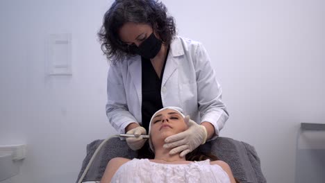 cosmetologist doing microdermabrasion procedure for woman in clinic