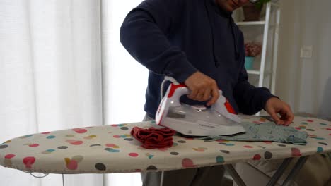 man taking wrinkled baby clothes and irons them. close up