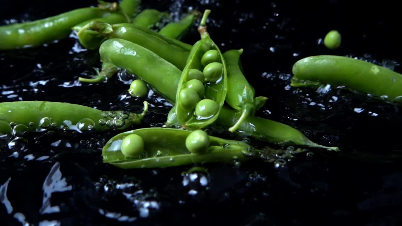 Falling of green peas in water on a black background. Slow motion