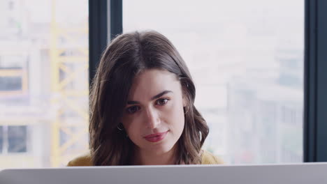 joven mujer blanca creativa mirando el monitor de la computadora en una oficina y bebiendo café, de cerca