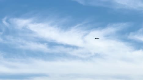 A lone jet flies through a clear sky, framed by delicate cloud patterns.