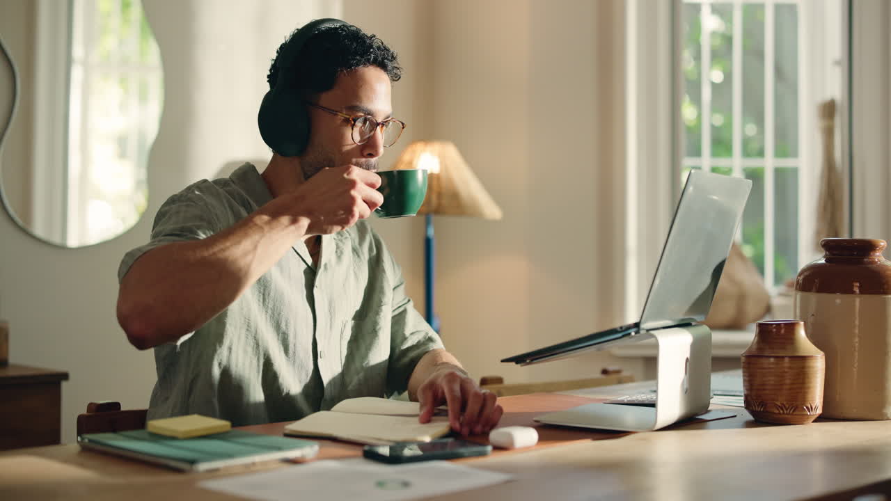 Uomo con le cuffie che lavora al laptop e prende appunti a casa