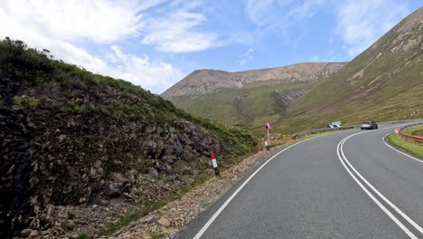 a car travels on a winding mountain road bordered by rocky hills under bright daylight, with smooth camera movement and a scenic, tranquil atmosphere
