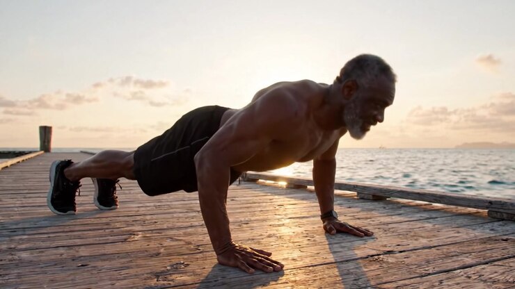 A Determined Older Man Engages in Push-Ups on a Dock by the Water Under a Beautiful Sunset, Showcasing Strength and Vitality Through Fitness