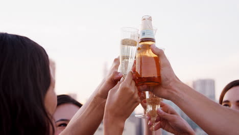 close up of friends with drinks making a toast on rooftop terrace with city skyline in background